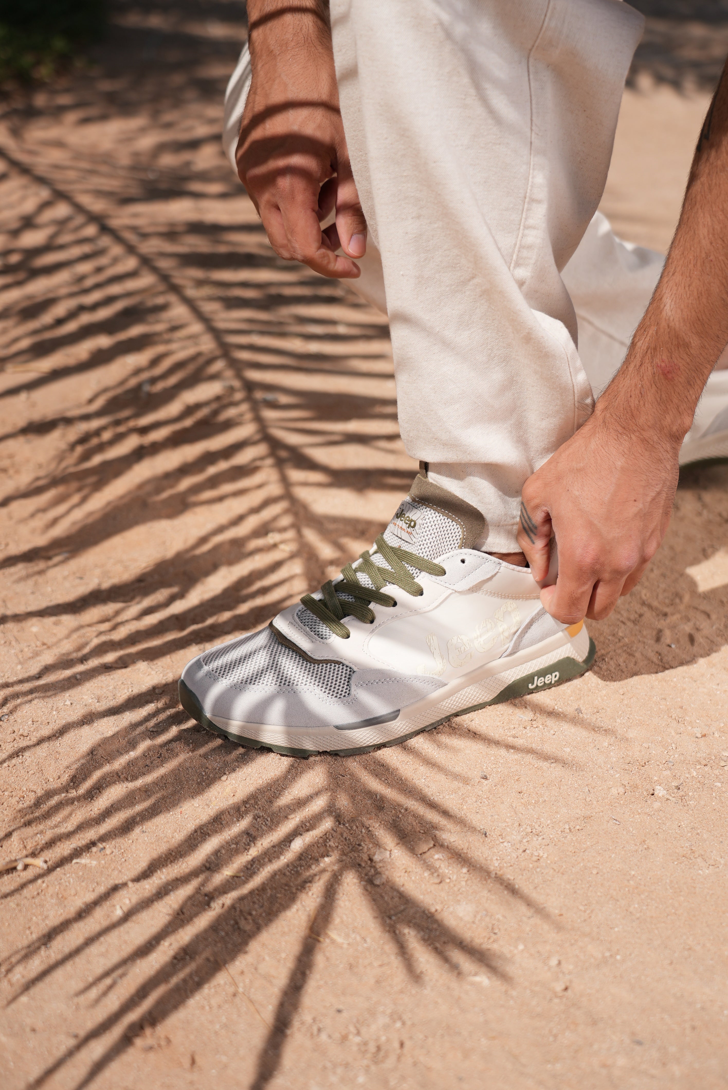 Man wearing a off-white Jeep sneaker with green accents on a sandy surface