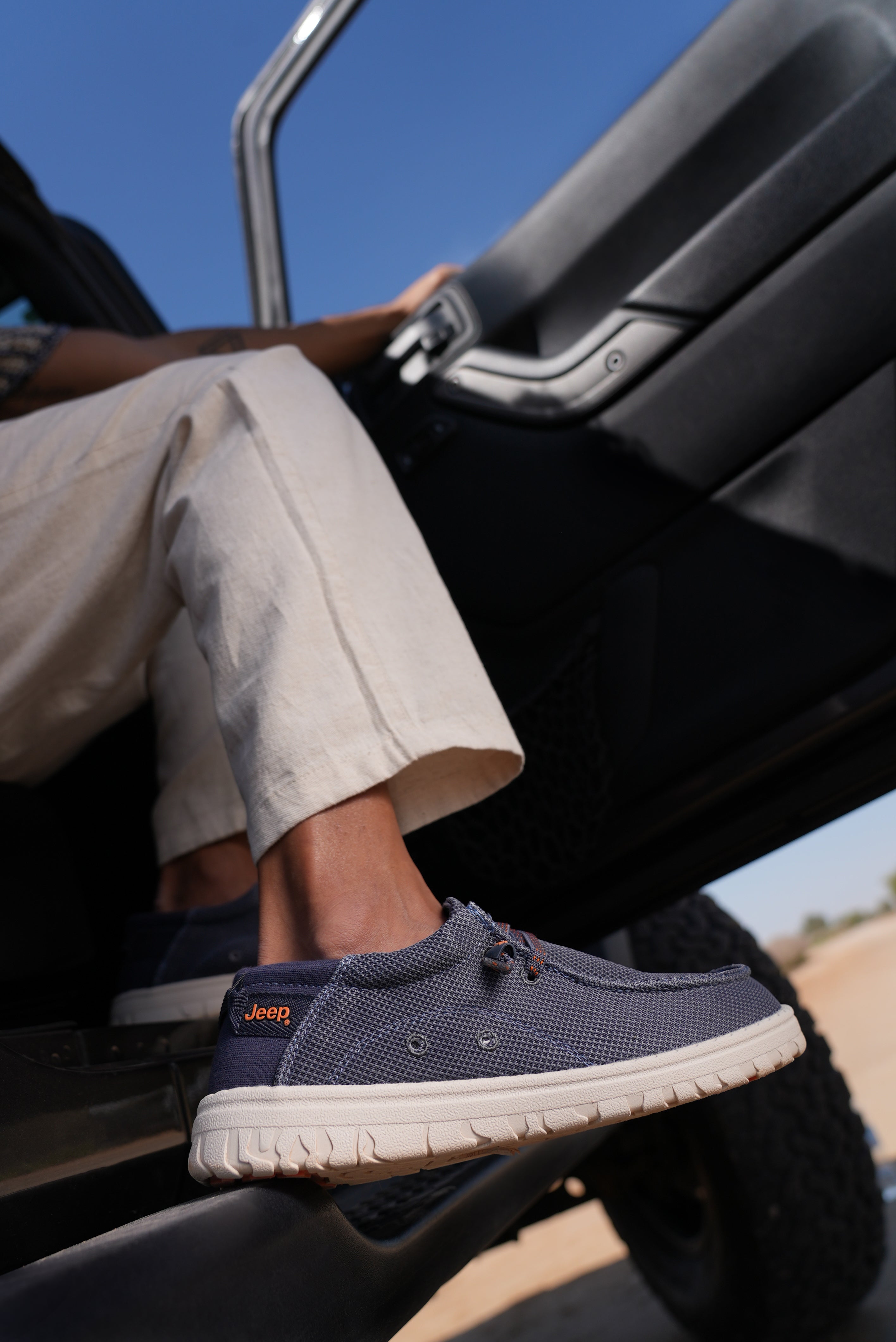 Man wearing navy blue wallabees with white soles, sitting inside a Jeep vehicle.