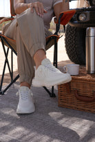 Person wearing off white Jeep sneakers sitting on a chair with a Jeep vehicle and picnic basket in the background.